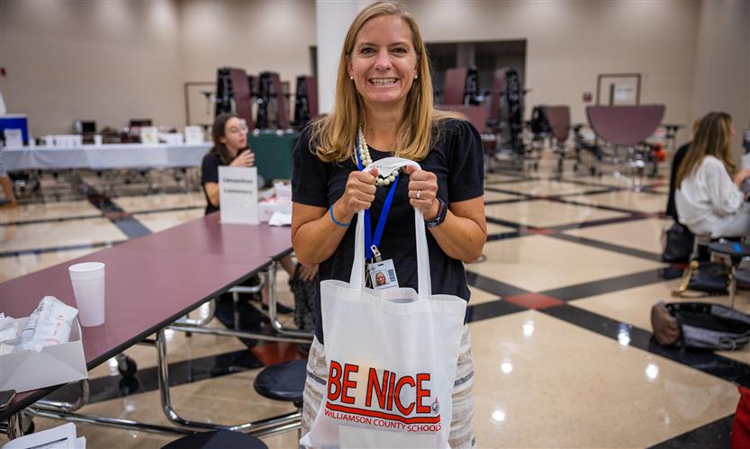 A woman grins while holding a bag that reads BE NICE in a cafeteria